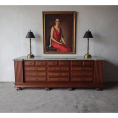 a painting hangs on the wall above a dresser with two lamps in front of it