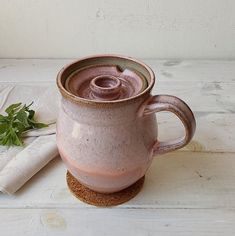 a pink mug sitting on top of a wooden table next to a napkin and sprig of parsley