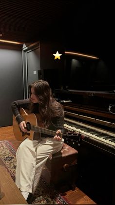 a woman sitting in front of a piano playing an acoustic guitar