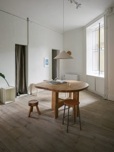 a table and chairs in a room with wood flooring, white walls and large windows