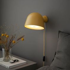 a lamp that is on the side of a bed next to a vase with flowers