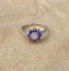 This beautiful opal and amethyst cluster ring has a 4.2mm round opal centre stone. With 8 round amethysts surrounding it measuring 2.25mm. Made from solid 925 sterling silver in Birmingham's historic Jewellery Quarter. The ring is available in a wide range of sizes. If your size isn't listed however please contact us and we will see if we can help you! There is a size conversion chart in our pictures!  If you are unsure of your ring size, you can order a ring sizer of us at https://etsy.me/33OVs Amethyst Cluster Rings With Gemstone, Amethyst Cluster Gemstone Rings, Cluster Amethyst Gemstone Rings, Cluster Amethyst Ring Gift, Cluster Amethyst Ring As A Gift, Gift Cluster Amethyst Ring, Spiritual Hallmarked Amethyst Ring, Amethyst Cluster Gemstone Jewelry, White Amethyst Ring For Anniversary