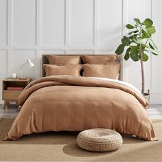 a bed with brown sheets and pillows in a room next to a potted plant