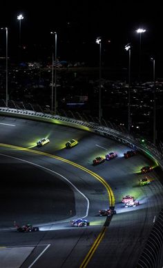 the cars are racing down the track at night time, with lights shining on them