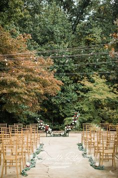 an outdoor ceremony setup with wooden chairs and greenery on the ground, surrounded by trees