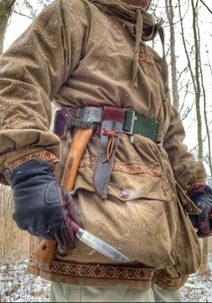 a man in an old outfit holding a knife and wearing winter clothing with snow on the ground