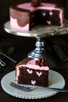 a piece of chocolate cake with pink frosting on a white plate next to a fork