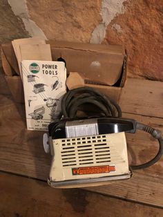 an old power tool sitting on top of a wooden table next to a box and wires