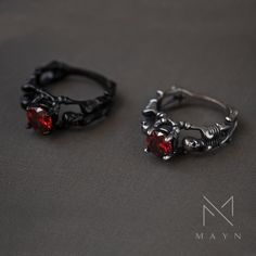 two rings with red stones on them sitting next to each other in front of a black background