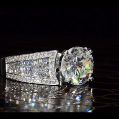 a diamond ring sitting on top of a reflective surface in front of a black background