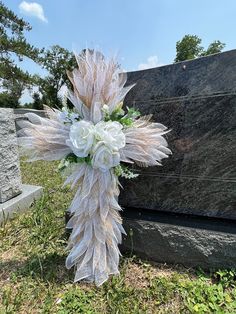 a cross made out of feathers and flowers sitting in the grass next to a grave