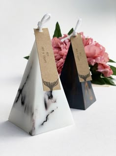 two small triangular shaped boxes with tags on them and pink flowers in the back ground