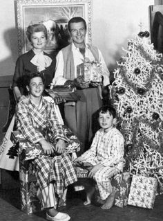 an old black and white photo of three people near a christmas tree with presents in front of them