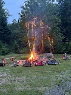 a campfire in the middle of a field with lots of camping gear around it