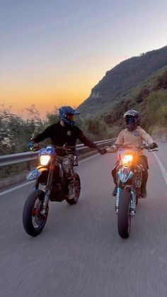 two motorcyclists are riding down the road at sunset with their helmets on