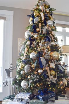 a decorated christmas tree with blue and silver ornaments on it in a living room next to a window