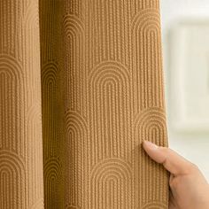 a hand is holding up the curtain in front of a window with an intricate pattern on it