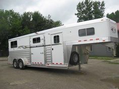 a white horse trailer parked in a parking lot next to a red and gray building