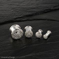 three different types of silver ear studs on a black stone surface, one with an intricate design