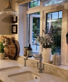 a kitchen sink with two faucets under a window next to potted plants