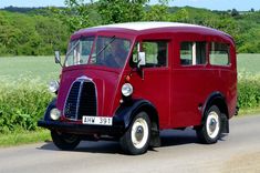 an old red bus is driving down the road in front of some green grass and trees