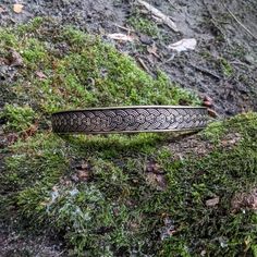 a metal bracelet sitting on top of a moss covered ground