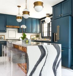 a kitchen with blue cabinets and marble counter tops in the center, along with two pendant lights hanging from the ceiling