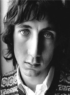 a black and white photo of a young man with long hair wearing a sweater looking at the camera