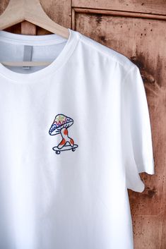 T-shirt blanc « FREE MUSHIE » EDITION LIMITÉE T-shirt (F/M) unisexe , brodé à la main, taille X-S-M-L-XL - 100% coton- tissus doux et de qualité.  Chaque pièce est réalisée avec un design artistique unique.  Démarquez-vous avec une tendance originale et trouvable nulle par ailleurs.  Hi, je suis Melissa, artiste dans le textile et illustratrice. Mon métier est  d'associer l'Art et la mode pour créer des pièces hors du commun et de  qualité. Les vêtements que je choisis sont recyclés ou neufs de haute qualité.  La liberté, la sagesse, l'humour et l'amour sont les valeurs que je souhaite partager.  Devenez aussi unique que mes créations.  Temps de création : 4 heures Instagram : @brodern.art Merci d'avoir visité mon profil <3. White Embroidered Logo T-shirt For Streetwear, White T-shirt With Embroidered Logo For Streetwear, White Embroidered Logo T-shirt For Summer, Custom Embroidered Cotton T-shirt For Streetwear, Relaxed Fit T-shirt With Embroidered Logo For Summer, Custom Embroidered Cotton Tops For Streetwear, Summer Cotton Shirt With Embroidered Logo, White Cotton Shirt With Embroidered Logo, White Embroidered T-shirt For Summer