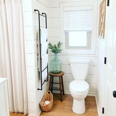 a white toilet sitting in a bathroom next to a wooden table with a vase on it