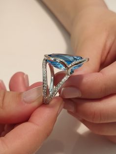 a woman is holding a blue ring with diamonds on it's sides and her hands