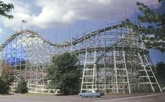 an amusement park roller coaster being built on the side of a road with cars parked in front of it