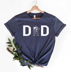 a t - shirt with the word dad printed on it, next to some leaves