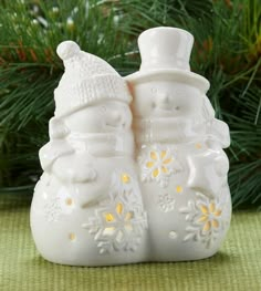 two white ceramic snowmen sitting next to each other in front of a christmas tree