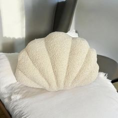 a white shell shaped pillow sitting on top of a bed next to a black chair