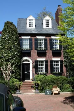 a large brick house with black shutters and white trim on the windows, surrounded by greenery