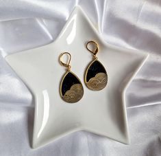 Dive into the world of serenity with these elegant dangling earrings. Inspired by Japanese seascapes, they feature a delicately chiseled golden wave pattern on a deep black background. Unique Features: Handcrafted: Each pair is carefully handcrafted, guaranteeing a unique and authentic piece of jewelry. Noble materials: High quality gold metal and black resin for a durable and refined finish. Timeless design: A perfect blend of Japanese tradition and modernity, for a look that is both elegant an Gold Teardrop Jewelry With Artistic Design, Gold Teardrop Earrings With Artistic Design, Japanese Jewelry, Wave Pattern, Black Backgrounds, Ideal Gift, Handcrafted Jewelry, Gold Metal, Timeless Design