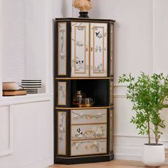 a tall black and gold cabinet with drawers in the corner next to a potted plant