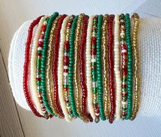 a stack of bracelets on top of a white cloth covered arm with red, green and gold beads