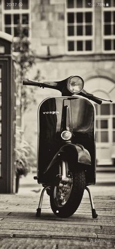 a black and white photo of a scooter parked in front of a phone booth