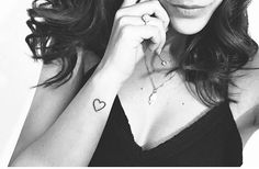 a woman with a heart tattoo on her left arm posing for a photo in black and white