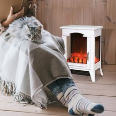 a cat laying on top of a blanket next to an open fire in a fireplace