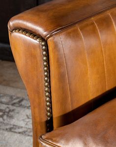 a brown leather chair with nail - studded arms and back rests on a carpeted floor