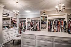 a walk in closet filled with lots of white drawers and clothes hanging on the walls