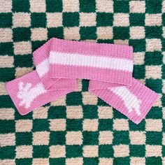 two pink knitted mittens sitting on top of a green and white checkered rug