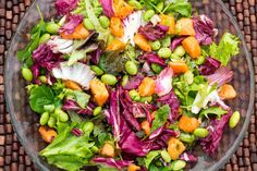 a salad with carrots, lettuce and peas in a glass bowl on a woven place mat