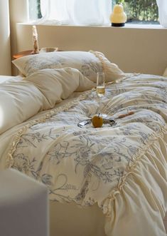 a bed with white comforter and pillows in front of a window, next to a glass of wine