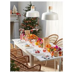 the table is set with plates, glasses and flowers in front of a christmas tree