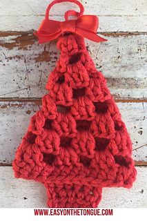 a red crocheted christmas tree ornament hanging on a white wooden wall