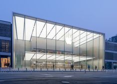 an apple store with glass walls and people walking around the outside area at night time